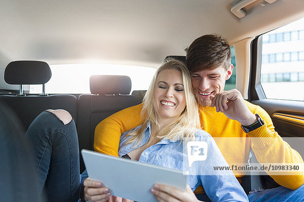 Glückliches Paar mit digitalem Tablett auf dem Rücksitz eines Autos