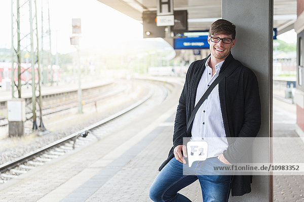 Lächelnder junger Mann wartet am Bahnsteig