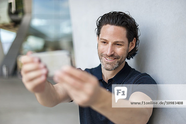 Porträt eines lächelnden Mannes  der sich selbst mit dem Handy fotografiert.