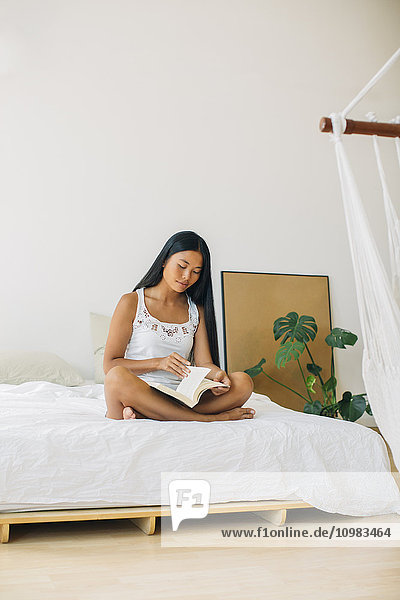 Junge Frau auf dem Bett sitzend Lesebuch
