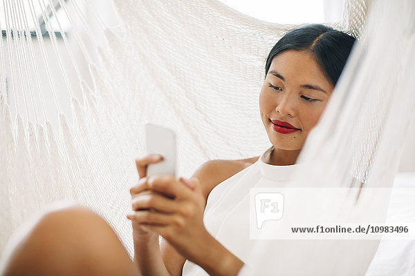Young woman in hammock using cell phone