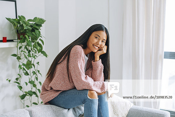 Lächelnde junge Frau auf der Rückenlehne der Couch zu Hause sitzend