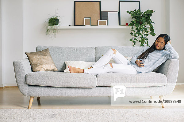 Young woman relaxing on couch in the living room using smartphone