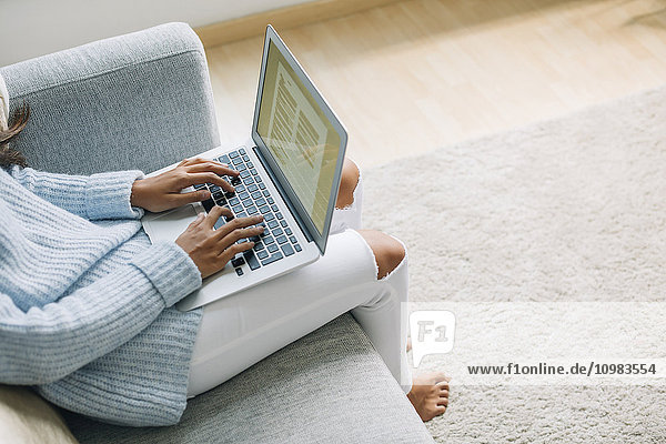 Junge Frau sitzend auf der Couch zu Hause mit Laptop  Teilansicht