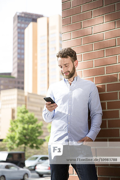 Lächelnder junger Mann mit Blick auf das Handy im Freien