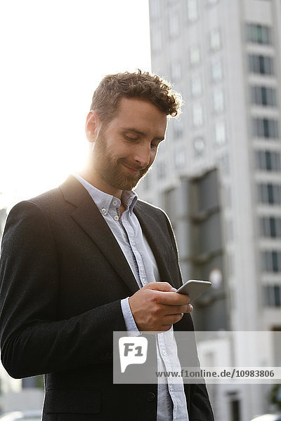 Smiling young businessman looking at cell phone outdoors