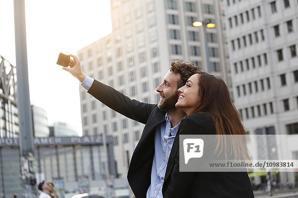 Lächelnder junger Geschäftsmann und Geschäftsfrau mit Selfie im Freien