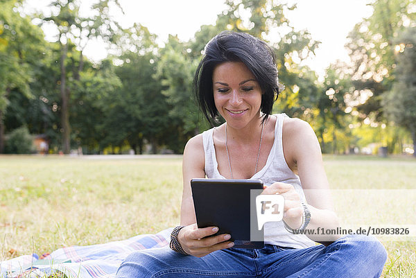 Smiling woman sitting on a meadow using tablet