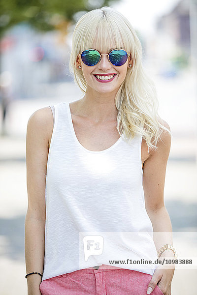 Porträt einer lächelnden blonden Frau mit verspiegelter Sonnenbrille