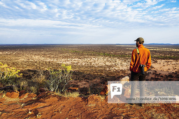 Namibia. Mann mit großer Kamera  der die weiten Ebenen der afrikanischen Savanne von einem Aussichtspunkt aus betrachtet