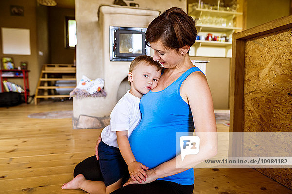 Kleiner Junge  der seine schwangere Mutter zu Hause umarmt.