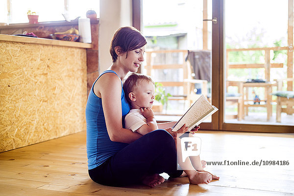 Schwangere Mutter schaut sich mit ihrem kleinen Sohn das Bilderbuch an.