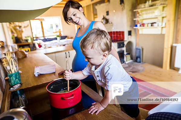 Kleiner Junge  der seiner schwangeren Mutter beim Kochen hilft.
