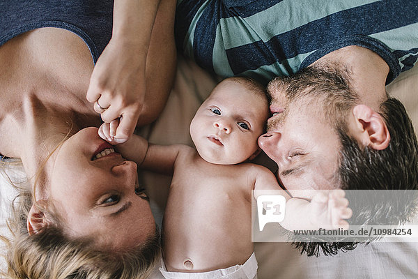 Mother and father with baby boy lying on bed
