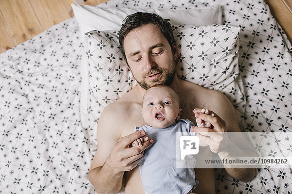 Father with baby boy lying on bed at home
