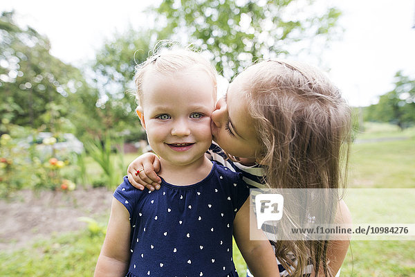 Mädchen küsst ihre kleine Schwester im Garten