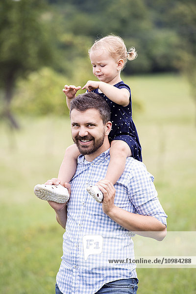 Glücklicher Vater trägt kleine Tochter auf den Schultern in der Natur