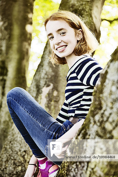 Porträt eines lächelnden Mädchens beim Klettern auf einem Baum