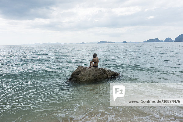 Thailand  Tubkaek  Rückansicht einer Frau  die auf einem Felsen sitzt und auf das Meer schaut.