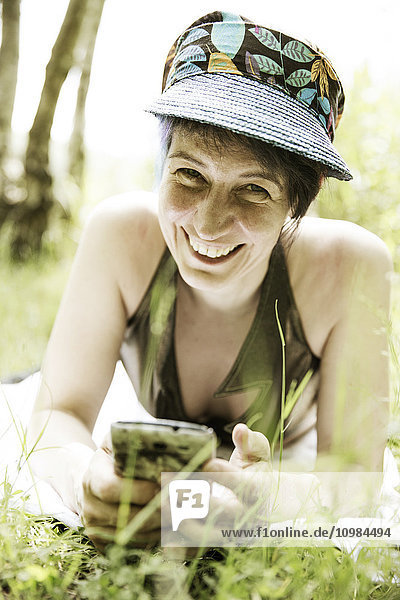 Porträt einer lachenden Frau auf einer Wiese mit Handy
