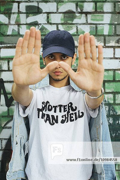 Porträt eines jungen Mannes im T-Shirt mit dem Spruch Heißer als die Hölle   der seine Arme ausstreckt.