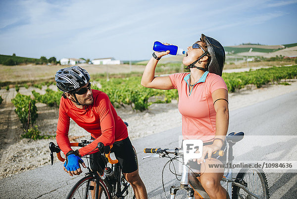 Spain  Andalusia  Jerez de la Frontera  couple of bikers drinking water on a rural road between vineyards