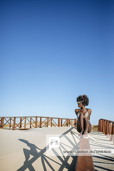 Junge Frau sitzt auf dem Geländer eines Gehweges am Strand
