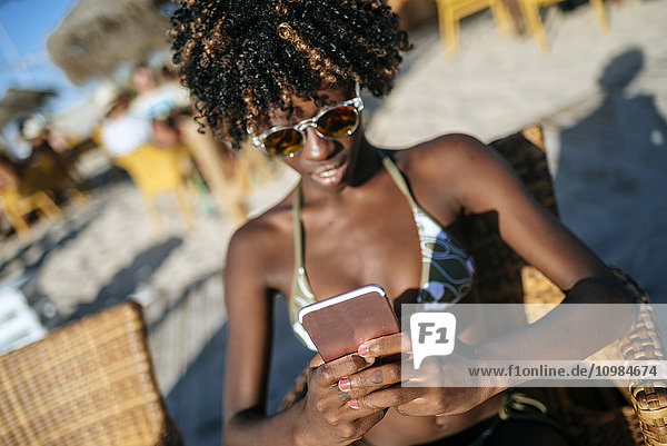 Junge Frau mit einem Smartphone in einer Strandbar