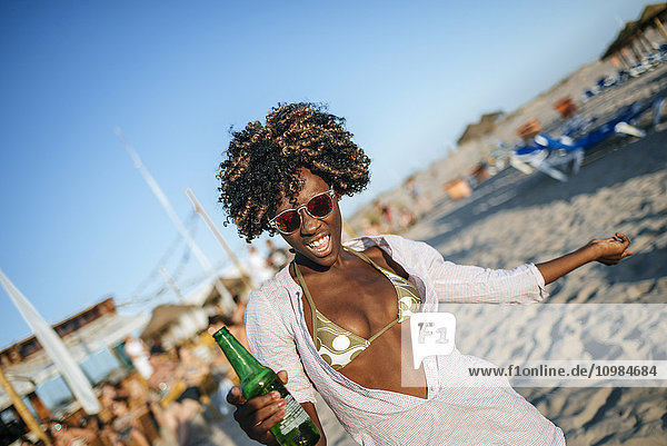 Junge Frau tanzt am Strand mit einem Bier in der Hand