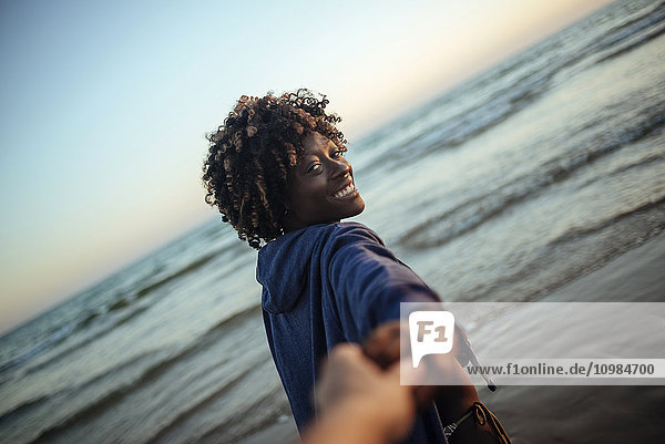 Junge Frau nimmt bei Sonnenuntergang die Hand eines Mannes am Strand.
