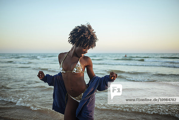 Fröhliche junge Frau  die bei Sonnenuntergang am Meer tanzt.