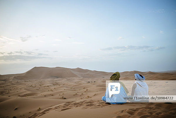 Frau sitzend in der Wüste mit Berberführer  Sonnenuntergang beobachtend