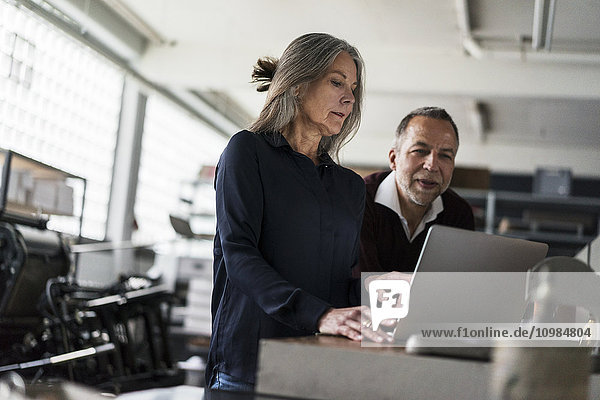 Senior Frau und Mann in einer Druckerei mit Blick auf Laptop