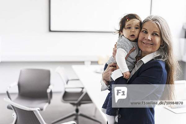 Senior businessswoman in conference room holding baby girl