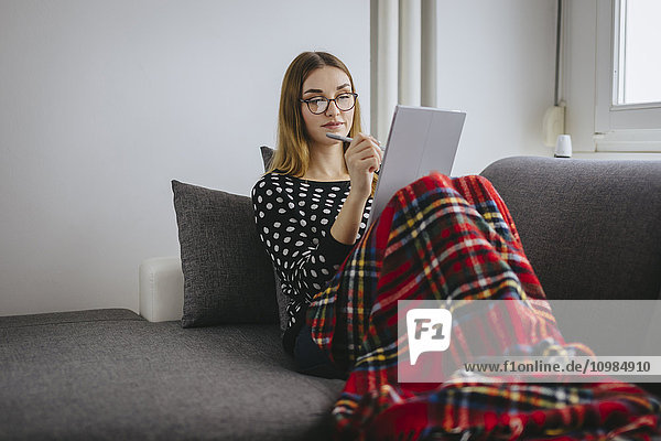 Young woman covered with blanket relaxing on the couch with her tablet