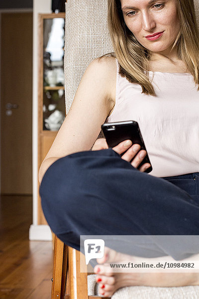 Woman sitting on chair at home looking at cell phone