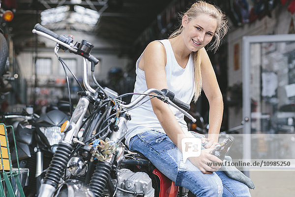 Lächelnde junge Frau mit Bierflasche auf dem Motorrad