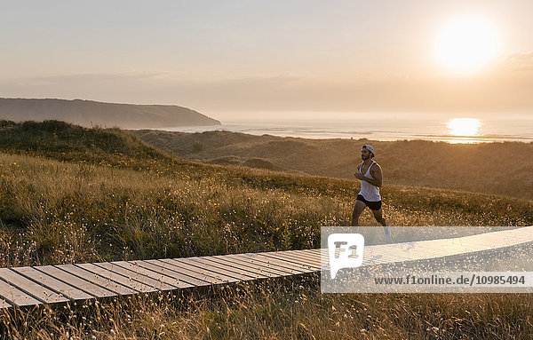 Spanien  Aviles  Sportler  der bei Sonnenuntergang einen Küstenweg entlang läuft.