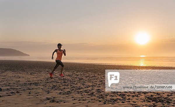 Athlete woman running on the beach at sunset