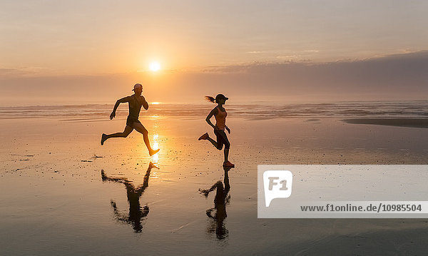 Sportlerpaar beim Laufen am Strand bei Sonnenuntergang