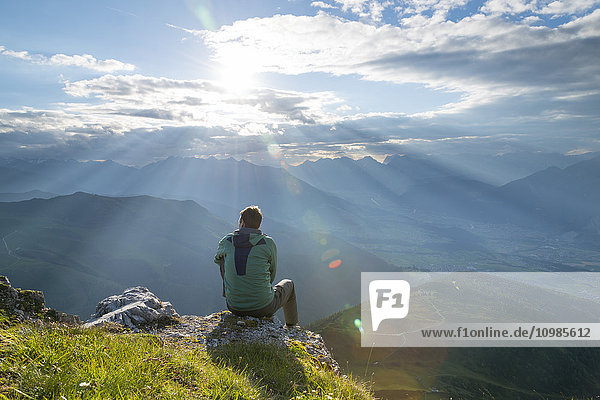Österreich  Tirol  Wanderer auf Aussichtspunkt gegen die Sonne sitzend