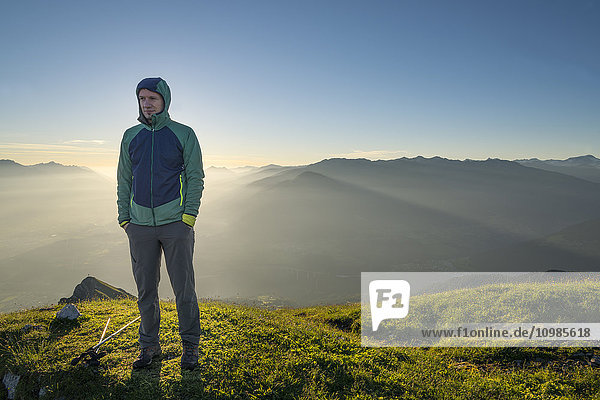 Österreich  Tirol  Wanderer bei Sonnenaufgang auf der Wiese stehend