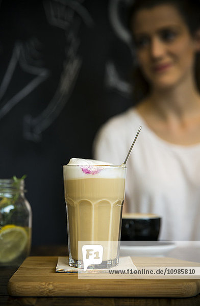 Glas Milchkaffee auf dem Tisch im Café mit junger Frau im Hintergrund