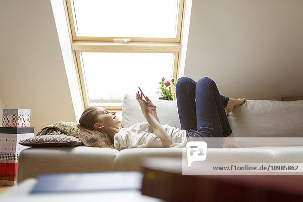 Entspannte Frau auf der Couch liegend mit dem Handy
