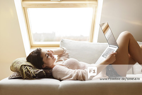 Relaxed woman lying on couch using laptop