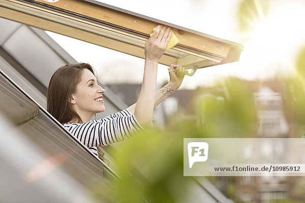 Lächelnde junge Frau putzt Dachfenster