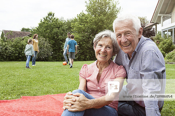 Porträt eines glücklichen Seniorenpaares mit Familie im Hintergrund im Garten