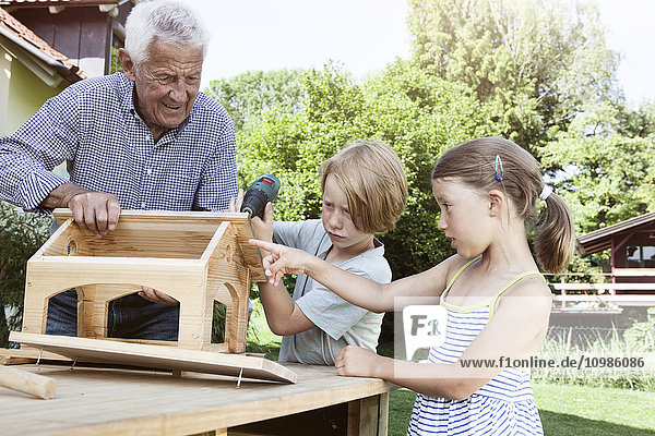 Großvater und Enkelkinder beim Bau eines Vogelhauses