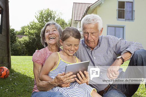 Großeltern und Enkelin im Garten mit digitalem Tablett