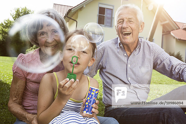 Großeltern und Enkelin im Garten  die Seifenblasen blasen.